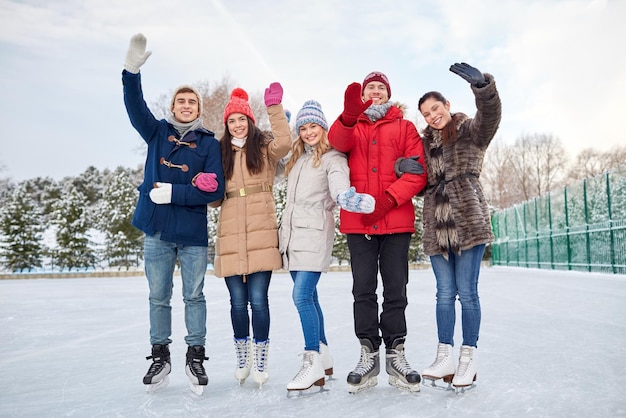 menschen, winter, freundschaft, sport- und freizeitkonzept - glückliche freunde eislaufen und winkende hände auf der eisbahn im freien