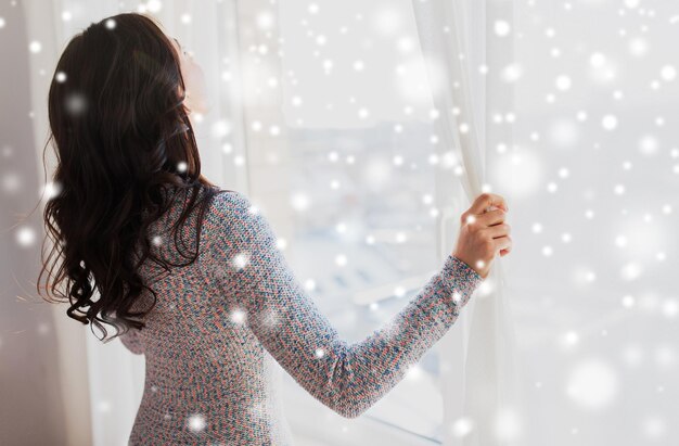 Menschen, Winter, Weihnachten und Heimkonzept – Nahaufnahme einer glücklichen Frau, die Fenstervorhänge über dem Schnee öffnet