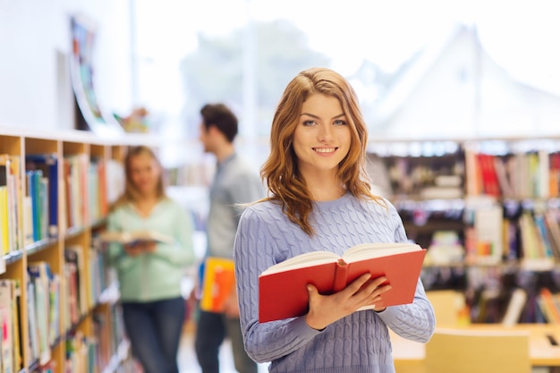 menschen, wissen, bildung und schulkonzept - glückliches studentenmädchen oder junge frau mit buch in der bibliothek