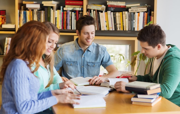 menschen, wissen, bildung und schulkonzept - gruppe glücklicher schüler, die bücher lesen und sich auf die prüfung in der bibliothek vorbereiten