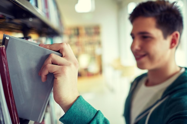 menschen, wissen, bildung und schulkonzept - nahaufnahme eines glücklichen studentenjungen oder jungen mannes, der bücher aus dem regal in der bibliothek nimmt