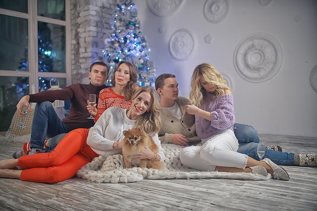 Menschengruppe und ein Hund im Silvesterinnenraum / Freunde von Jungen und Mädchen Weihnachtsabend mit Sekt