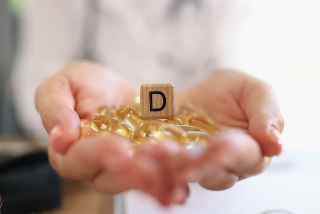 Menschliche Hände halten Stapel von Vitamin-D-Kapseln mit Holzwürfel mit D-Symbol aus nächster Nähe