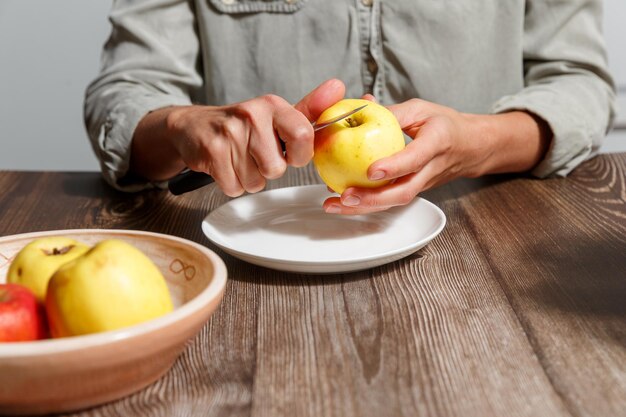 Menschliche Hände schälen einen Apfel in einer Küche mit einem Messer über einem hölzernen Hintergrund. Konzept für gesunde Ernährung und Veganismus