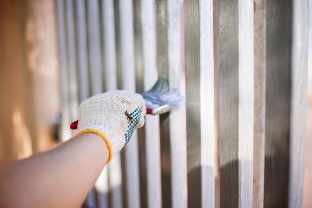 Menschliche Hand bemalt einen Hauszaun, indem er die Farbe des Stahlzauns auffrischt. Nahaufnahme einer Hand mit Handschuh und Pinsel. Frische, nasse Silberfarbe