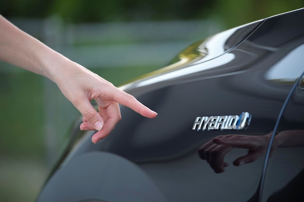 Menschliche Hand, die ein Hybridautoschild auf einem neuen effektiven Fahrzeug zeigt