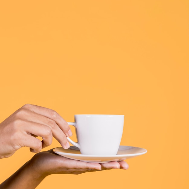 Menschliche Hand, die weiße keramische Kaffeetasse und Untertasse hält