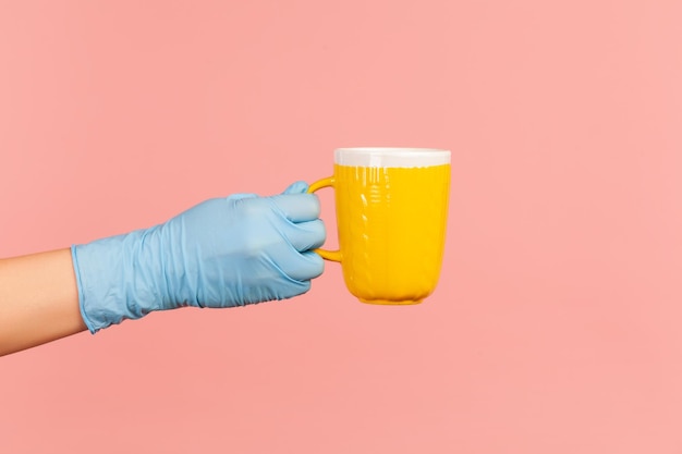 Menschliche Hand in blauen OP-Handschuhen, die eine gelbe Tasse heißes Getränk in der Hand halten und zeigen.