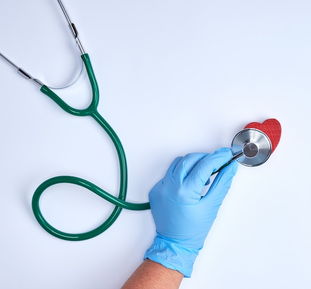 Menschliche Hand in den blauen sterilen Handschuhen, die ein grünes Stethoskop halten