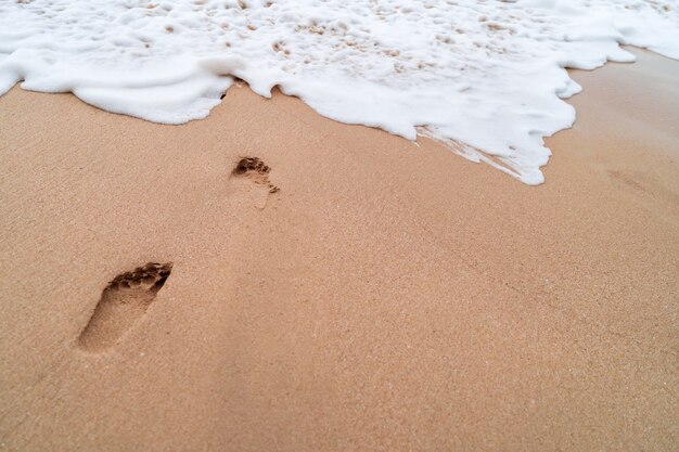 Menschlicher Fußabdruck auf tropischem Strandhintergrund des Sandesommers.