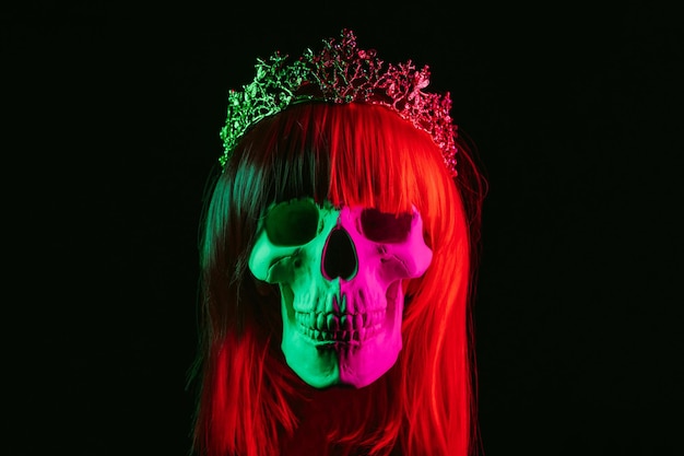 Menschlicher Schädel einer Frau in einer Perücke mit roten Haaren in einer Krone mit einem farbigen rosa grünen Licht