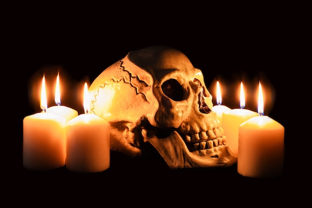 Menschlicher Schädel im Profil unter brennenden Kerzen im dunklen, gruseligen Stillleben, Altar.