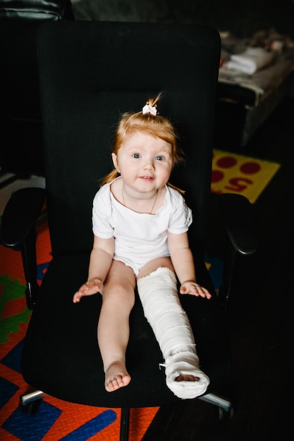 Menschliches Gesundheits- und Medizinkonzept Kind mit Verband am Bein Fersenbruch oder gebrochener Fußknochen Kleines Mädchen verletzt, das zu Hause auf dem Stuhl sitzt Nahaufnahme