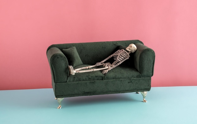 Menschliches Skelett liegt auf einer grünen Samtcouch auf rosa und blauem Hintergrund Burnout und Depression Minimal Art Posterkonzept