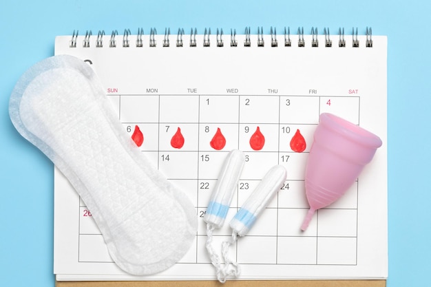 Menstruation Slipeinlagen mit Tampons und einer Menstruationstasse auf dem Hintergrund des Kalenders