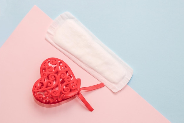 Menstruationsbinden liefert mit rotem Herz auf Papierhintergrund