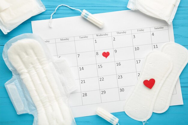 Menstruationskalender mit Tampons und Pads aus Baumwolle auf blauem Hintergrund. Frauenkritische Tage, Frauenhygieneschutz. Menstruationsbeschwerden