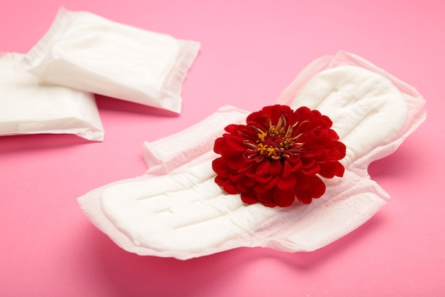 Menstruationstampons und -pads auf rosa Hintergrund. Eine Rosenblüte liegt auf einer Menstruationsunterlage. Menstruationszyklus. Hygiene und Schutz. Ansicht von oben. Vertikales Foto