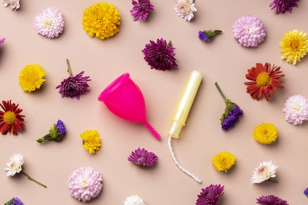 Menstruationstasse und Tampons auf Blumenmusterhintergrund