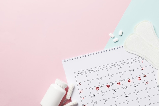 Menstruationszykluskalender auf rosa Hintergrund. Tabletten und Tampons, Binden. Eisprung Konzept. Menstruationskonzept.