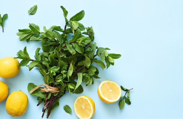 Foto menta fresca y limones para hacer limonada en una mesa azul.