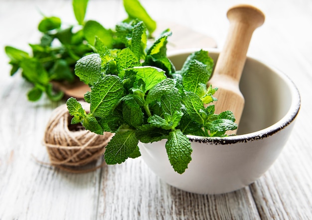 Menta verde fresca en mortero sobre superficie de madera blanca