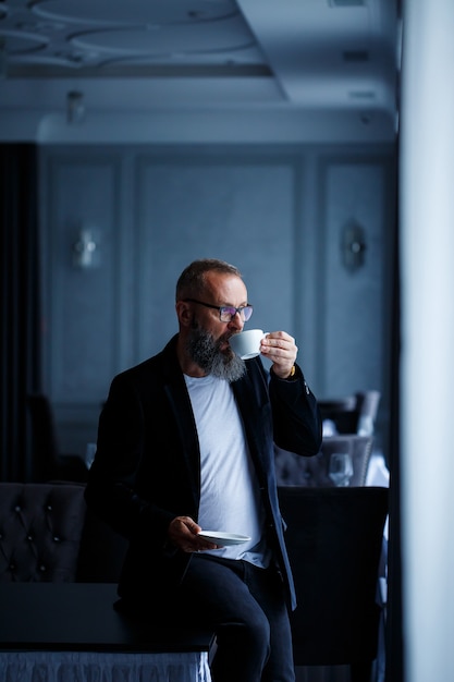 Un mentor, director, hombre de negocios adulto con gafas y traje toma café y descansa. Concepto de jornada laboral