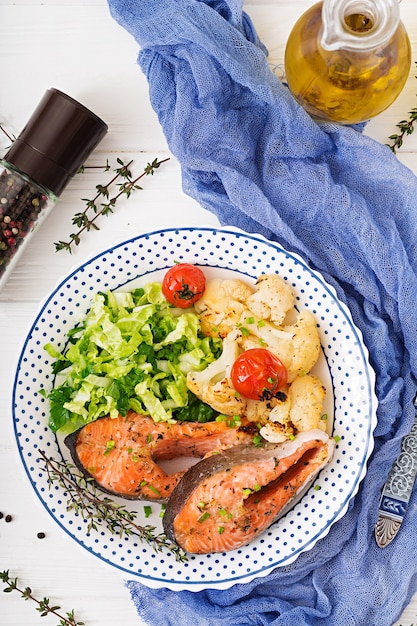 Foto menu dietético. bife salmon cozido com couve-flor, tomates e ervas.