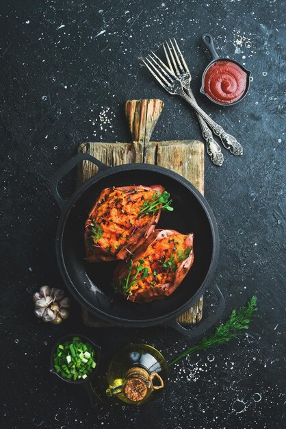 Menu vegetariano Batata-doce assada com especiarias e alho em uma panela Comida saudável em um fundo de pedra preta