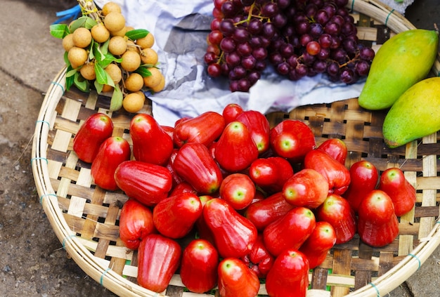 Foto mercado asiático de agricultores callejeros que vende fruta fresca en hoi an, vietnam. manzana rosa, longan, uva y mango. principalmente colores rojos.