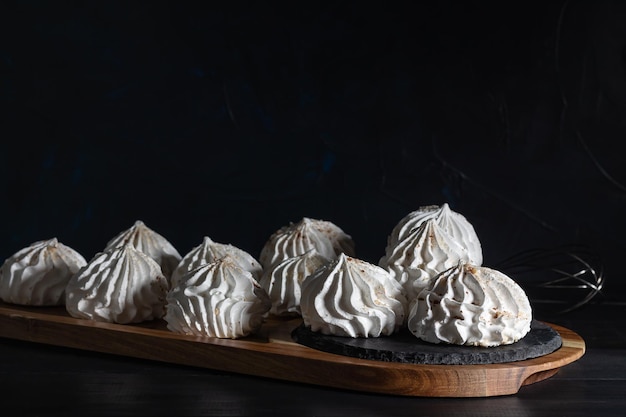 Merengue de baunilha branca em tábua de madeira em fundo escuro foco seletivo cozinha baixa chave em casa