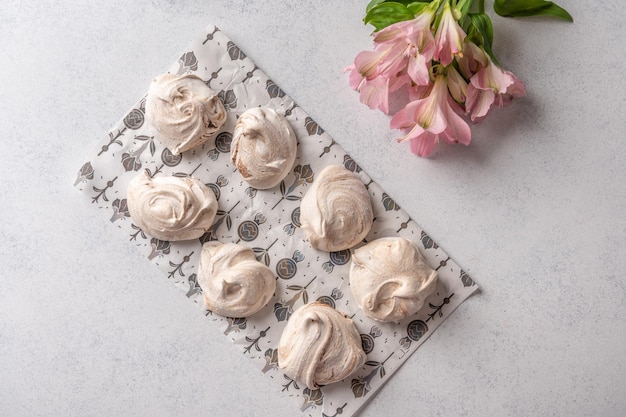 Merengue de sobremesa de ovos populares caseiros em um papel de pastelaria sobre fundo claro ao lado do topo da flor rosa