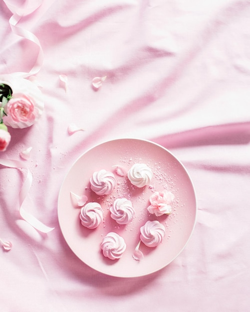 Merengue dulce en un plato rosa Rosas en un jarrón blanco sobre un mantel rosa Lugar para la etiqueta