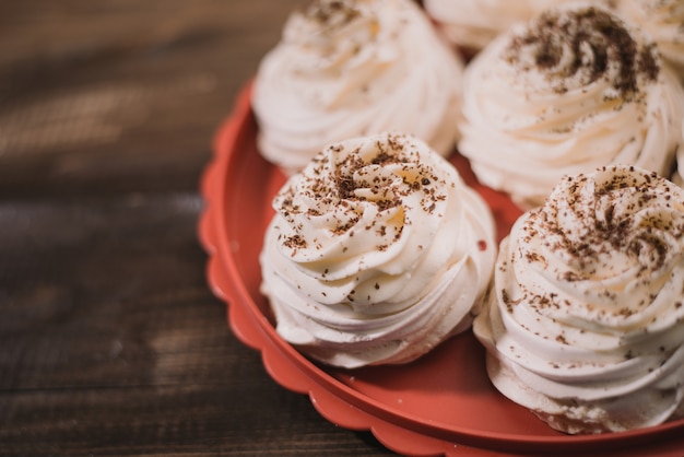 Merengue Pavlova de cor creme encontra-se em uma bandeja vermelha sobre uma mesa de madeira velha. Receita de doces de merengue com cobertura em chocolate