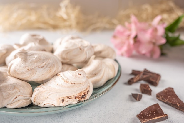 Merengue de postre de huevos populares caseros en un plato sobre un fondo claro junto a una flor rosa y