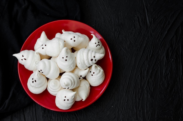 Merengues de Halloween fantasmas com calda de chocolate no prato sobre um preto. Ideia de comida para festa de halloween.