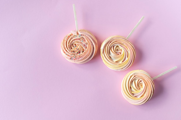 Merengues dulces redondos rosas en un palo con decoración sobre un fondo rosa