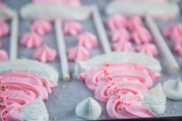 Merengues en forma de sombreros navideños rosas con pompón y una solapa blanca en un palo sobre blanco