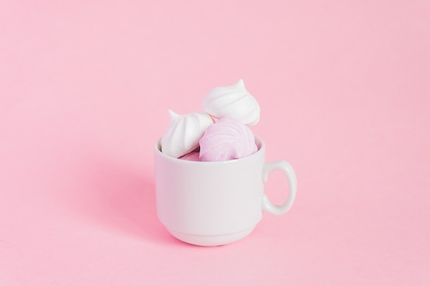 Merengues retorcidos blancos y rosados en una pequeña taza de café de porcelana en rosa