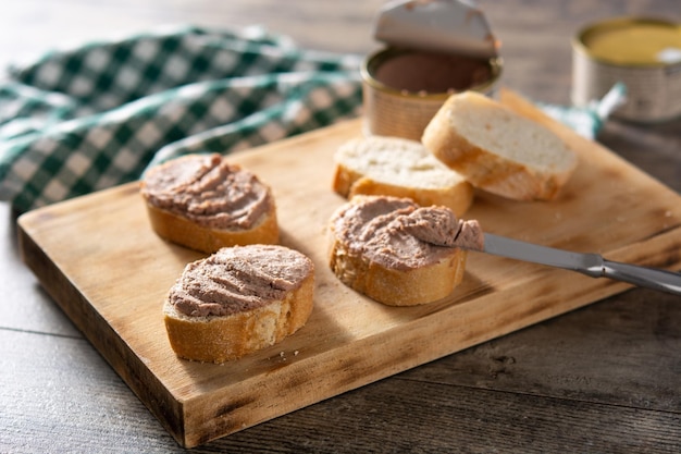 Mergulhando o pão torrado com patê de fígado de porco na mesa de madeira