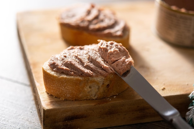 Mergulhando o pão torrado com patê de fígado de porco na mesa de madeira