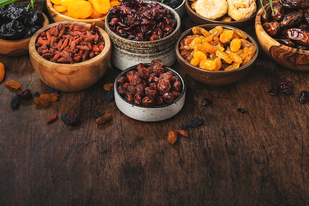 Merienda de alimentos saludables frutos secos naturales secados al sol mezcla orgánica de albaricoques secos higos pasas dátiles arándanos cerezas bayas de goji ciruelas pasas en tazones sobre fondo de madera vista superior