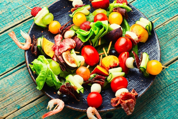 Merienda festiva de gambas jamón frutas y verduras en brochetas de madera