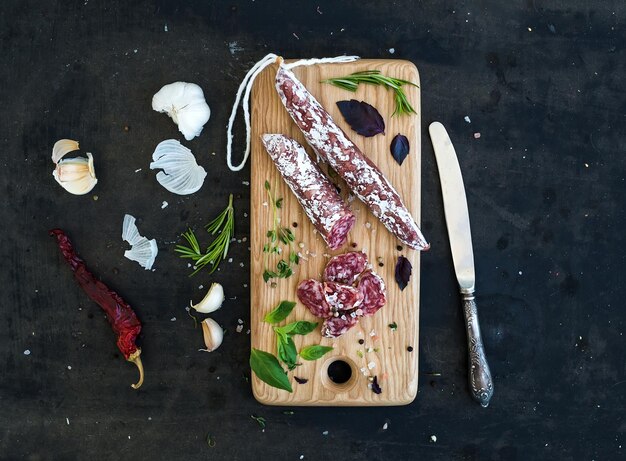 Merienda gourmet de carne, salami, ajo y hierbas en una tabla de madera rústica sobre un fondo grunge oscuro