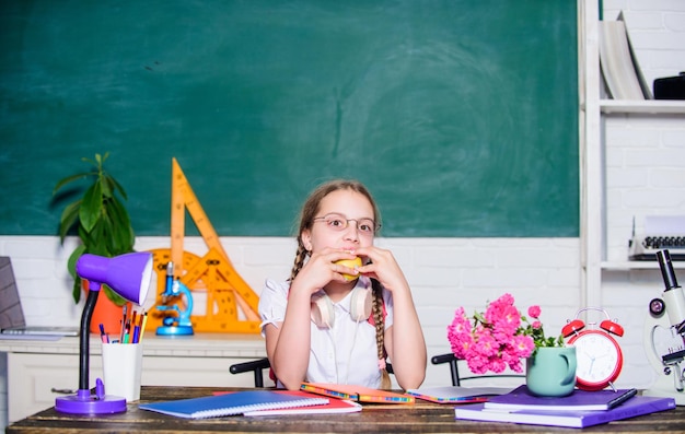 Merienda entre lecciones Colegiala sentarse escritorio pizarra fondo Niño estudiante en la escuela Niña niño pequeño comiendo manzana fruta Concepto de vida escolar Estilo de vida saludable Infancia moderna Vacaciones escolares