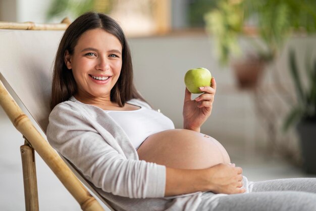 Foto merienda saludable hermosa mujer embarazada sentada en una silla y sosteniendo manzana verde