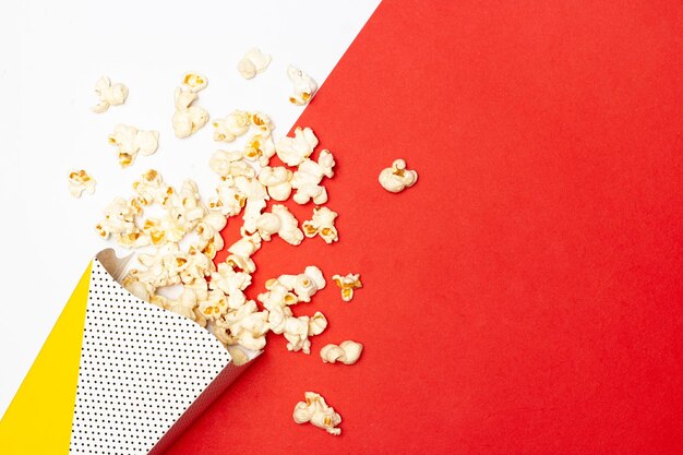 Merienda de ver el concepto de película Las palomitas de maíz dulces flotan fuera de la taza de papel sobre fondo rojo y blanco