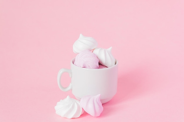 Meringues retorcidos brancos e rosa em uma pequena xícara de café de porcelana em fundo rosa sobremesa francesa