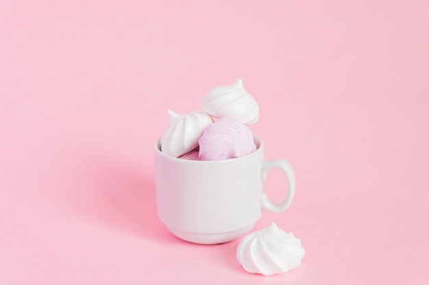 Meringues retorcidos brancos e rosa em uma pequena xícara de café de porcelana em fundo rosa sobremesa francesa