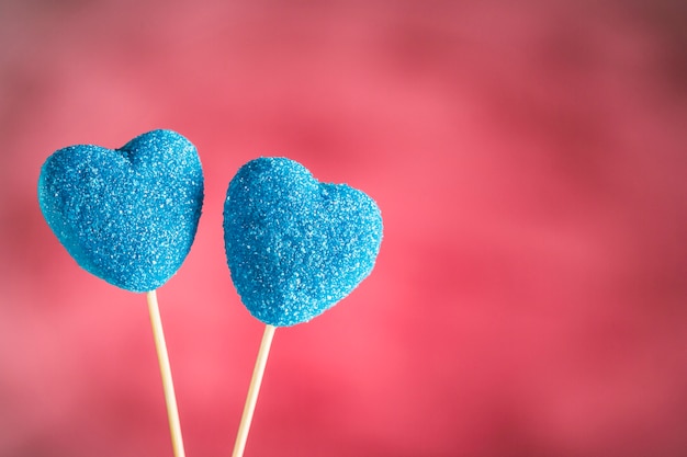 Mermelada en azul de azúcar en forma de corazones en palos sobre un fondo rosa claro